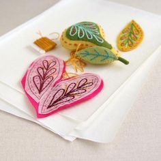 two felt hearts are sitting on a piece of white paper next to a leaf ornament