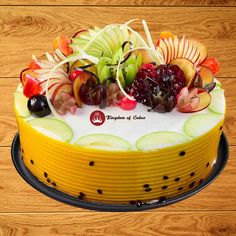 a cake with apples, grapes and cherries on top is sitting on a wooden table