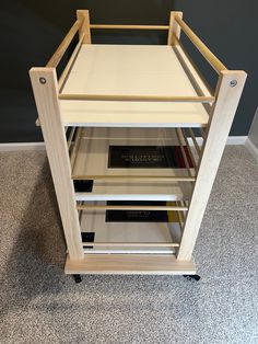 a wooden shelf with books on it in the middle of carpeted floor next to wall