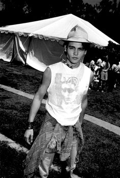 black and white photograph of a young man with a hat on his head standing in front of a tent