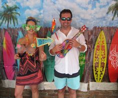 a man and woman standing next to each other in front of surfboards wearing sunglasses