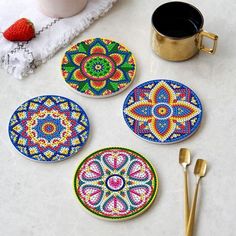 four coasters with colorful designs on them next to a cup and spoon, strawberries