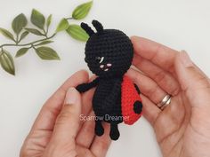 a crocheted black cat with a red heart in it's paws sitting next to a plant