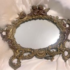 an ornate mirror with cherubs on it is sitting on a white cloth covered bed