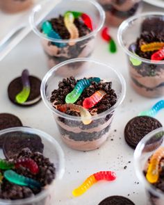 there are many desserts in plastic cups on the table with candy worms and oreos