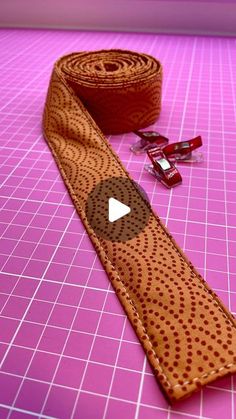 a video demonstrating how to sew a tie on a pink background with scissors and tape