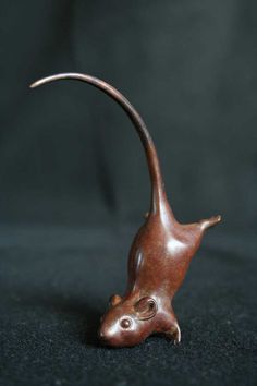 a small figurine of a mouse on a black surface with its tail curled up