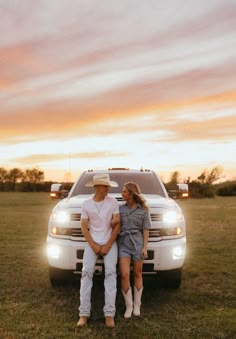 a man and woman sitting on the back of a truck in a field at sunset