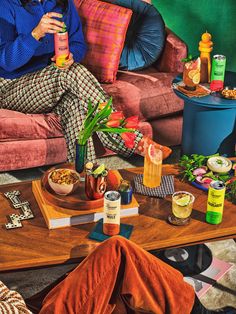 a woman sitting on a couch holding a bottle in front of her face while surrounded by food and drinks