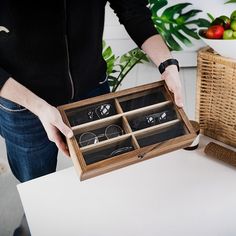 a person holding an open wooden box filled with rings and bracelets on top of a table