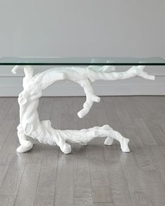 a glass table topped with white branches on top of a hard wood floor next to a wall