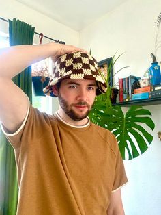 a man wearing a hat standing in front of a window with his hands on his head