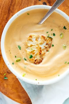 a white bowl filled with soup on top of a wooden table next to a spoon