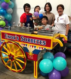 a group of people standing in front of a colorful cart with balloons and streamers