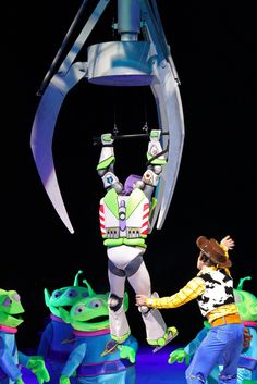 two people are performing on stage in front of an alien costume and some other characters