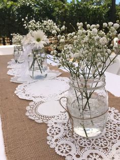 white flowers are in mason jars on a burlock tablecloth with lace doily