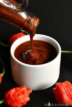 someone pouring sauce into a white bowl with red peppers around it on a black surface