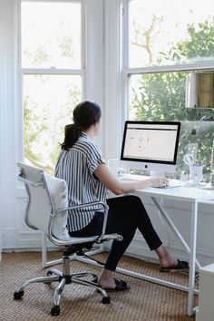 a woman sitting at a desk with a computer in front of her, looking out the window