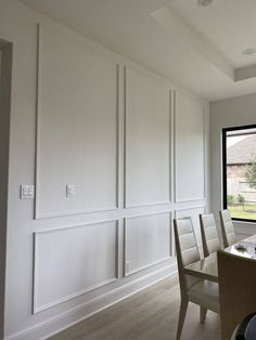 a dining room table and chairs in front of a window with white paneling on the walls