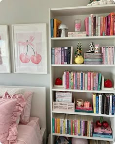 a white book shelf filled with lots of books next to a pink bed and pillows