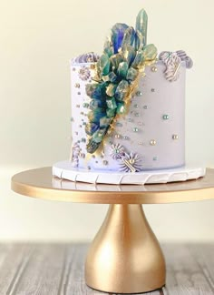 a white and blue cake with flowers on top sitting on a gold plated stand