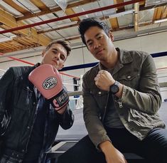 two men sitting next to each other with boxing gloves on their hands and one wearing a pink glove