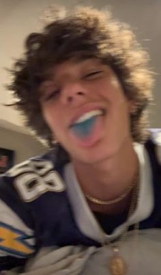 a young man is brushing his teeth while wearing a football jersey and gold chain necklace