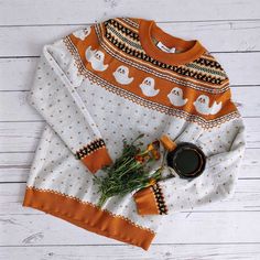 an orange and white sweater with ghost print on it next to a cup of coffee