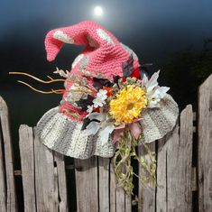 a knitted hat on top of a wooden fence with flowers in the center and a flower bouquet attached to it