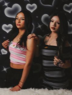 two beautiful young women standing next to each other in front of a heart wallpaper