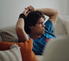 a young man laying on top of a couch holding his head in his hands and looking down