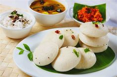 some food is sitting on a white plate with green leaves and bowls in the background