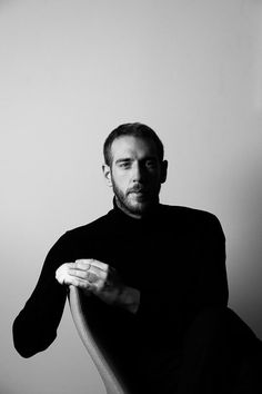 a black and white photo of a man sitting in a chair with his hand on the arm