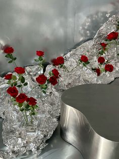 some red roses are in a glass vase on tin foil and another is sitting next to it