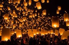 many people are flying lanterns in the sky at night time with bright lights on them