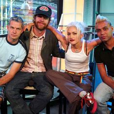 three men and a woman sitting next to each other in front of a store window