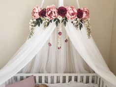 a white crib with pink and red flowers hanging from it's canopy over the bed