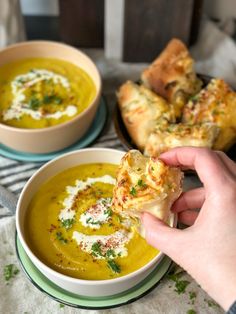 a person is holding a piece of food in front of a bowl of soup and bread