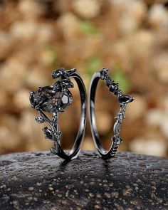 two wedding rings sitting on top of a rock in front of a rocky area with leaves and flowers