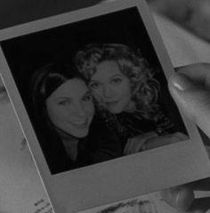 a person holding up a polaroid with two women on it's back and one woman smiling at the camera