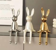 three gold and silver rabbit figurines sitting on top of a counter next to each other