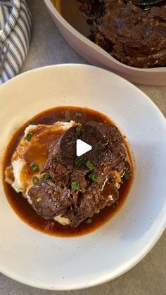 a white plate topped with meat and gravy next to a casserole dish