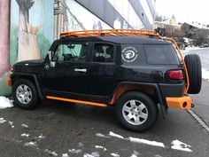 an orange and black jeep is parked in front of a building with graffiti on it