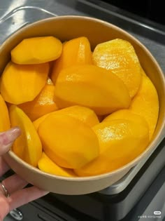 a person holding a bowl full of cut up mangoes on top of a stove