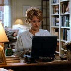 a woman sitting in front of a laptop computer on top of a wooden desk next to a lamp