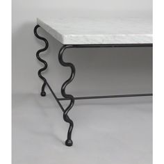 a white marble top table with black iron legs and an intricate design on the base