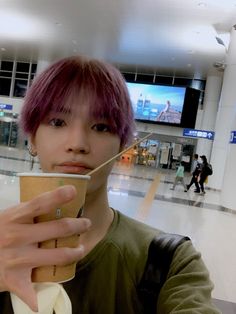 a person with pink hair holding a drink in their hand and looking at the camera