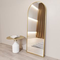 a large mirror sitting on top of a wooden floor next to a white vase and table