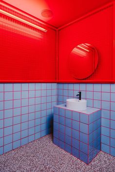 a blue and red tiled bathroom with a round mirror on the wall above the sink