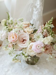 a vase filled with lots of pink and white flowers on top of a lace covered table cloth